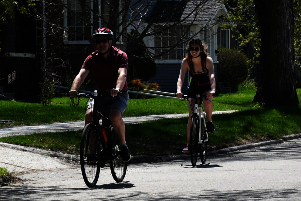Man and woman riding single file down a calm residential street.