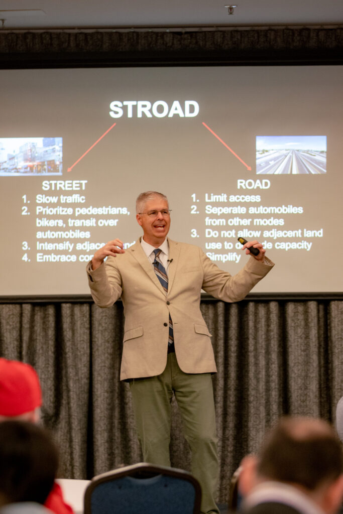 Charles stands in front of the screen describing a stroad.