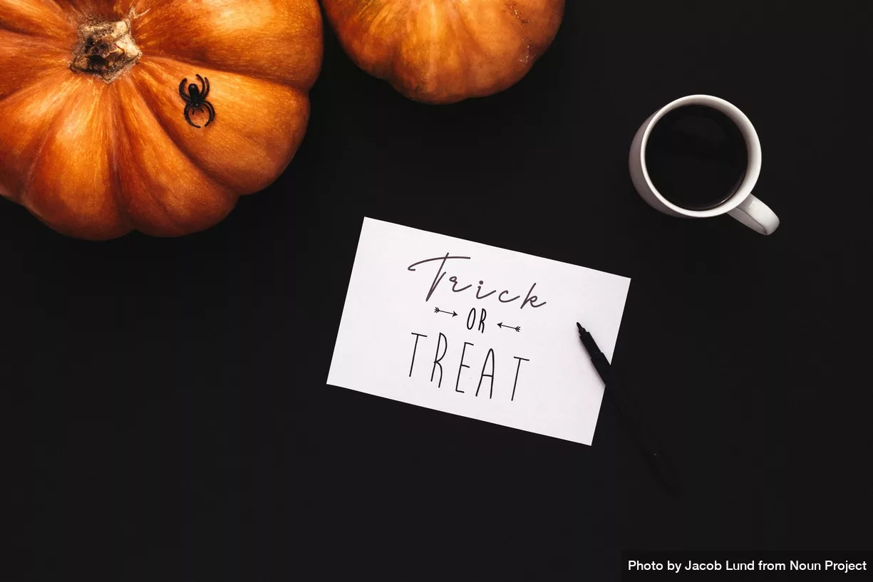 trick or treat written on white card near pumpkins on black surface - photo by by Jacob Lund from Noun Project