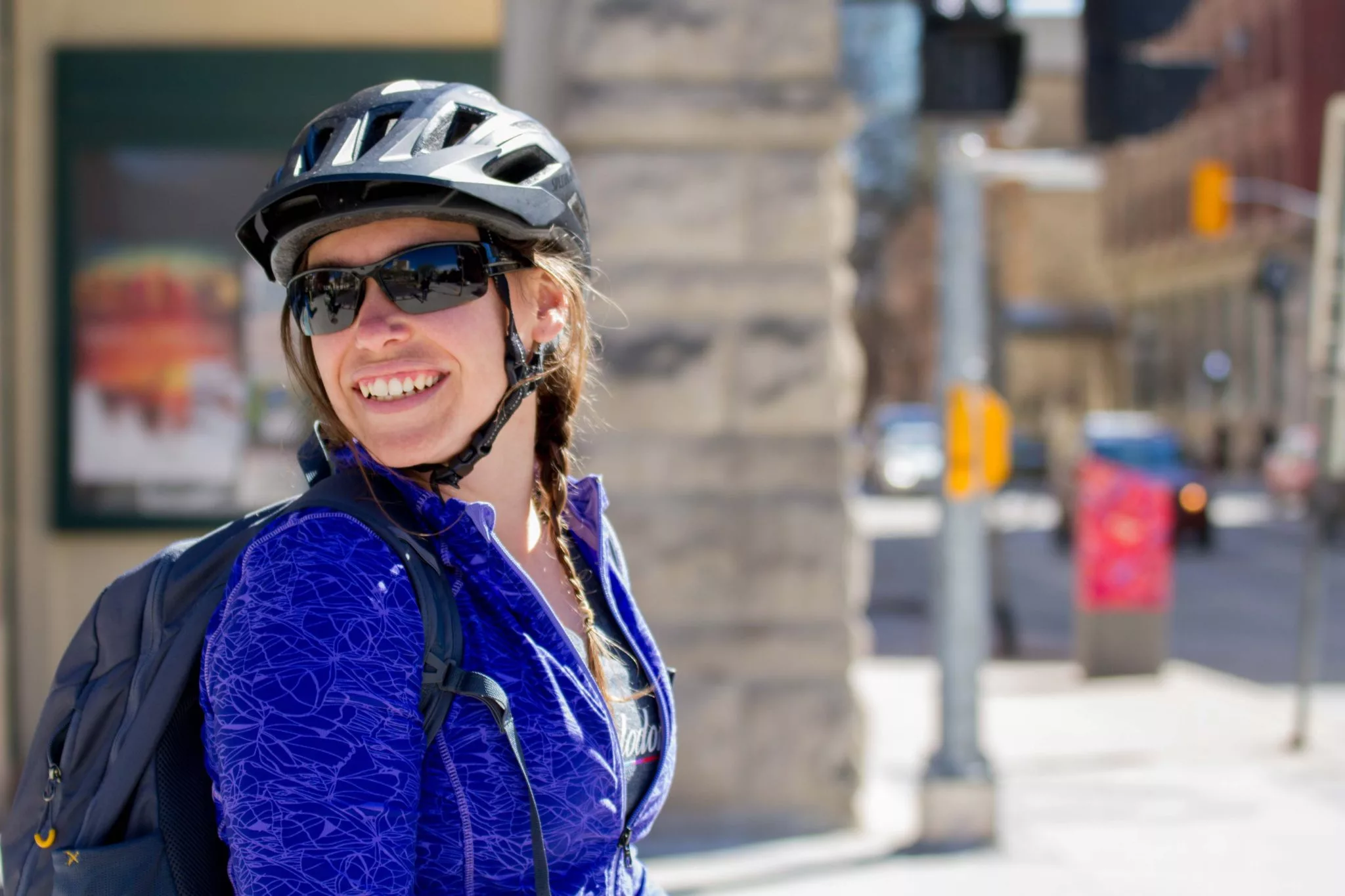 woman wearing a helmet and sunglasses as she looks over her shoulder at a crosswalk