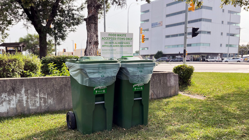 Picture of two large compost bins on the grass with trees and an apartment building in the background.