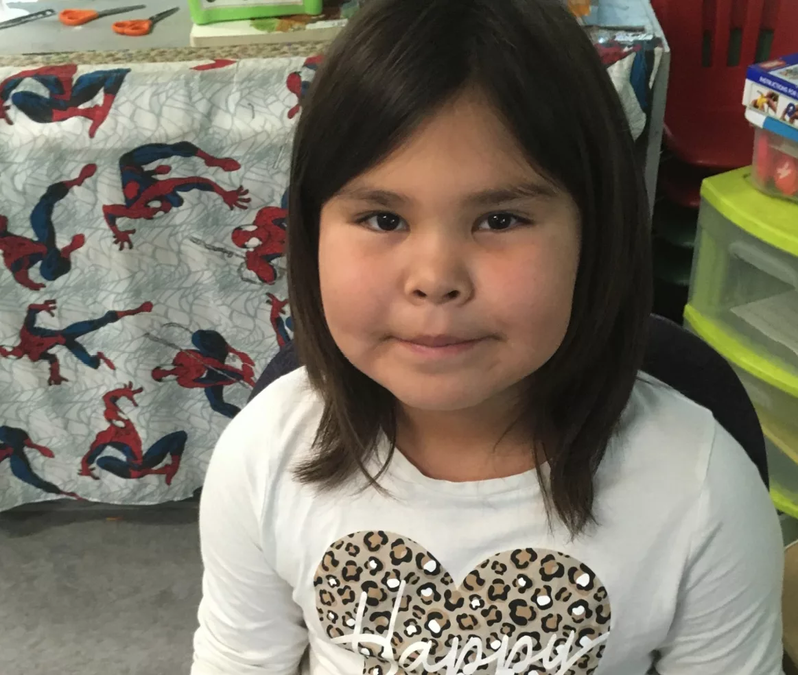 young girl with shoulder length hair, she's wearing a long sleeved shirt with the word happy on it