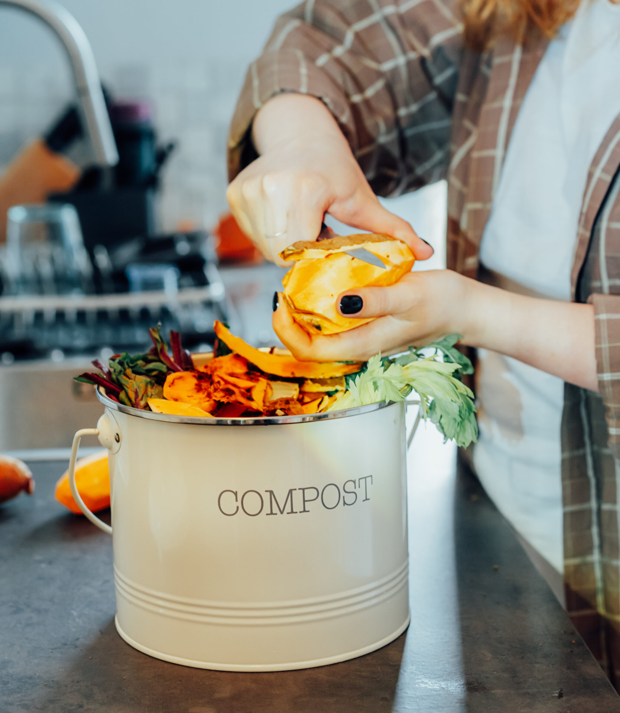 Woman in kitchen adding vegetables to a small composting container.