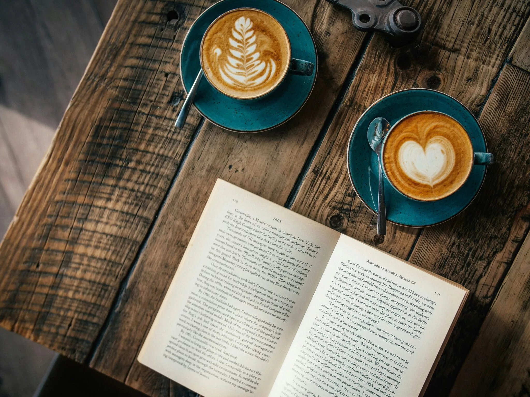 book laying open on a wooden surface next to two cups of latte