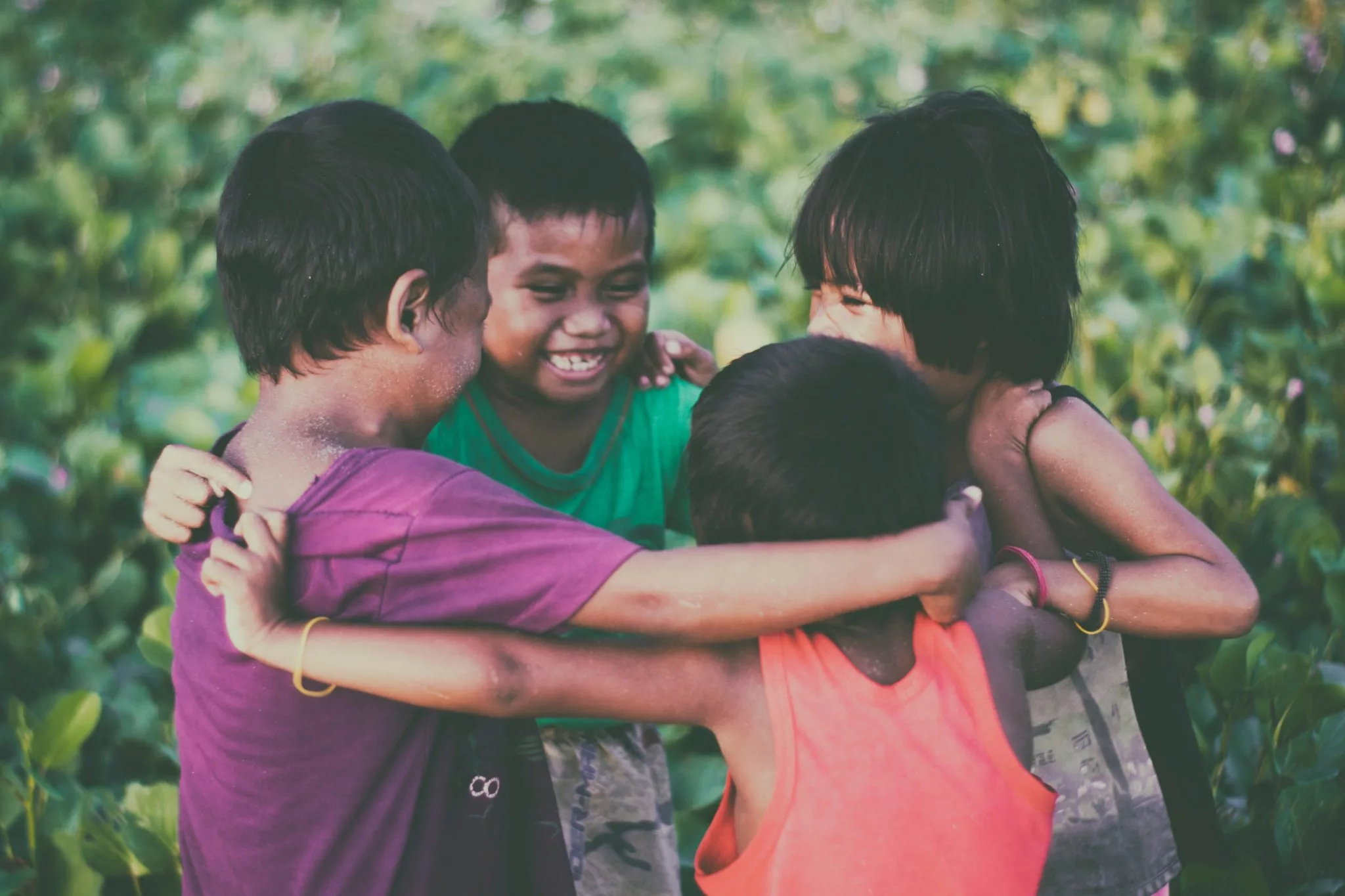 adorable group of young children giving each other a group hug while smiling and laughing outside