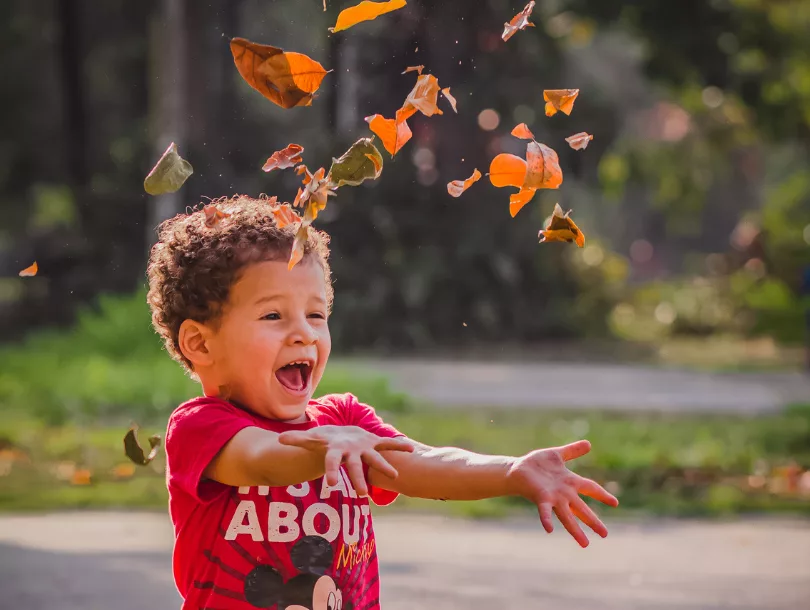 smiling boy throwing leaves in the air