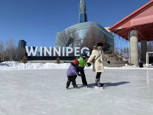 parent and two children holding hands as they ice skate in front of the museum for human rights