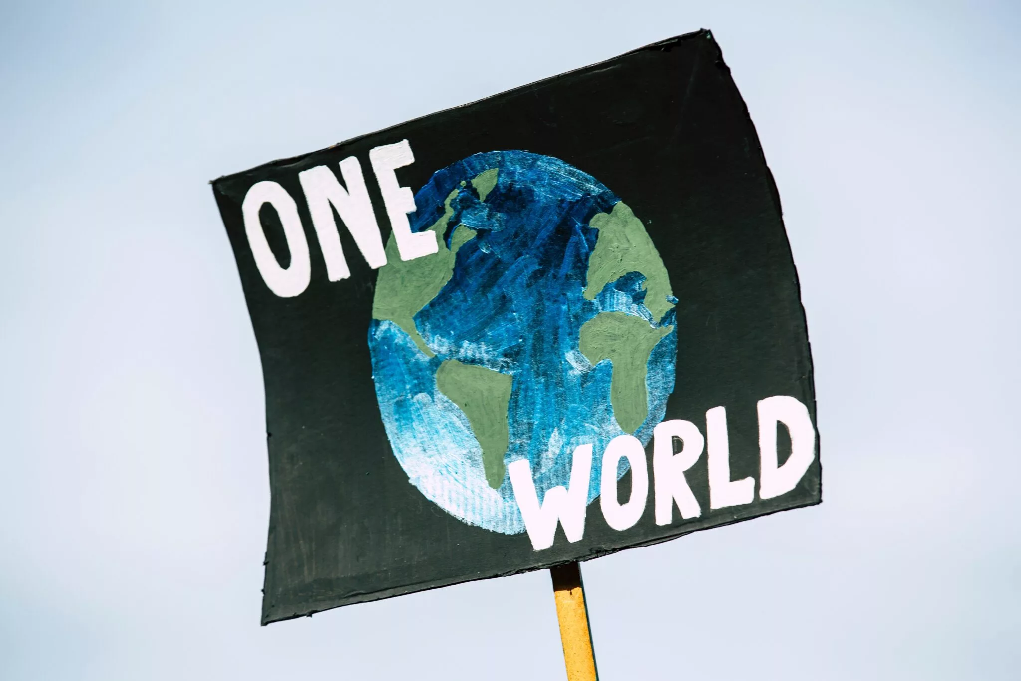 hand painted cardboard sign of earth with bold font reading One World