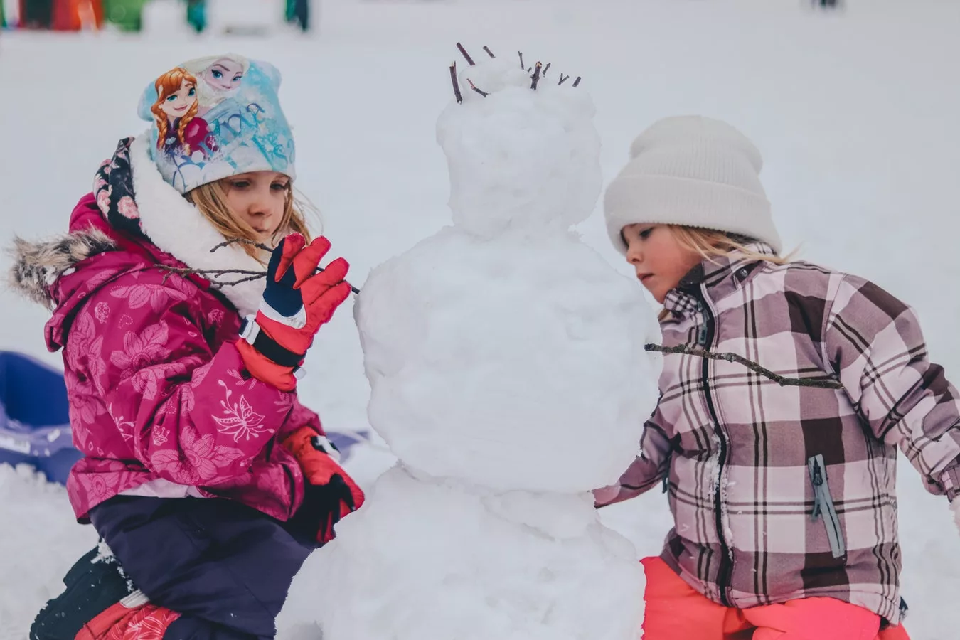 two children dressed in winter outer wear playing with a snowman