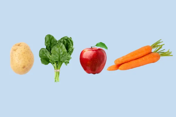 An image of a potato, a bunch of spinach, an apple, and carrots on a plain background.